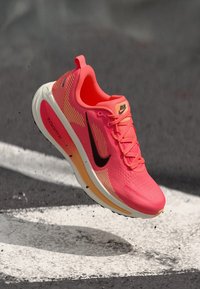Αθλητικό παπούτσι Nike για τρέξιμο σε φωτεινό ροζ, με επάνω μέρος από υφασμάτινο πλέγμα, μαύρο λογότυπο swoosh και λευκή σόλα, με πορτοκαλί λεπτομέρειες και αυλάκια.