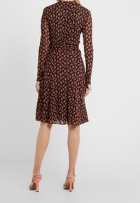 Svart långärmad klänning med ett röd och orange blommönster, utsvängd kjol och halvgenomskinligt material. Matchad med rosa klacksandaler.