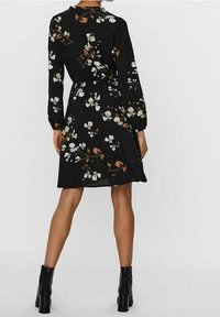 Musta kukkamekko pitkillä hihoilla, kireällä vyötäröllä ja valkoisella sekä ruskealla kukkakuviolla. Yhdistettynä mustiin korkokenkiin.