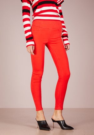 Donna che indossa pantaloni skinny rosso acceso, mules nere con tacco alto a punta e una maglia a maniche lunghe a righe rosse, bianche e nere.