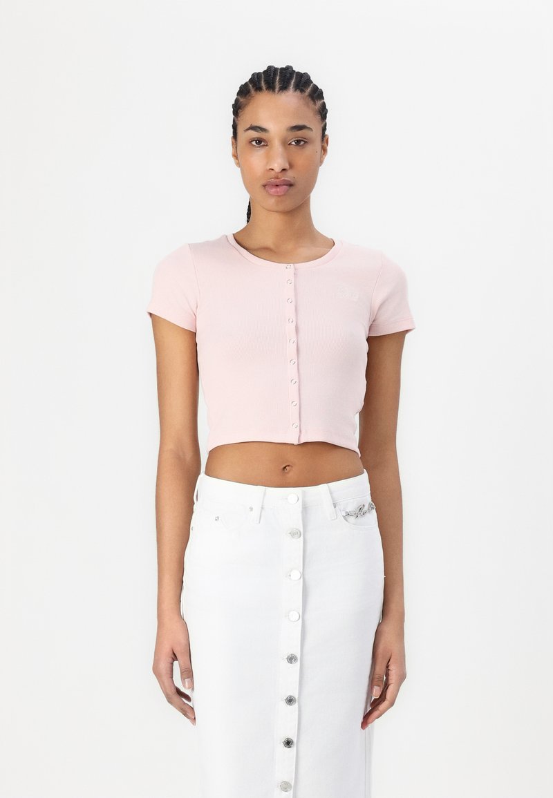 Top corto a coste rosa con maniche corte e bottoni frontali, abbinato a una gonna di jeans bianca alta in vita con chiusura a bottoni.