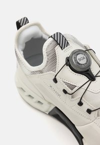 Viegls sporta apavi off-white krāsā ar teksturētu režģi augšdaļā, BOA šņoru sistēmu un melniem akcentiem uz papēža un cilpas.