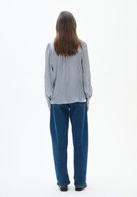 Randig långärmad skjorta med skräddarsydda detaljer, ihopparad med löst sittande blå jeans och svarta skor, sedd bakifrån.