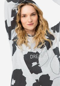 Witte netstof hoodie met zwart bloemmotief; heeft een capuchon, lange mouwen en de tekst "DREAMS". Lichtgewicht, ademend materiaal.