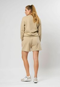 Beige sweatshirt en bijpassende shorts, gemaakt van zacht materiaal. Casual fit met ribgebreide boorden. Gemaakt met lichte sneakers, haar in een staart.