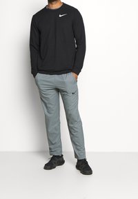 Camisa negra de manga larga de Nike con un logo blanco, combinada con joggers grises claros de Nike que tienen un bolsillo lateral y detalles negros. Zapatillas negras.