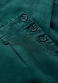 Teal katoenen stof met een gladde textuur, voorzien van drie donkere knopen en een geplooid ontwerp op de tailleband.