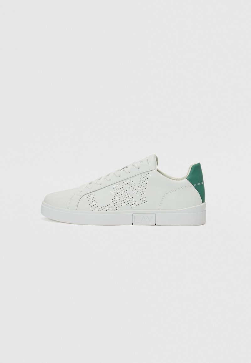 Weiße Sneaker mit perforiertem Muster, grünem Fersenakzent, glattem Leder, runder Zehenpartie und flacher, weißer Sohle. Minimalistisches Design.