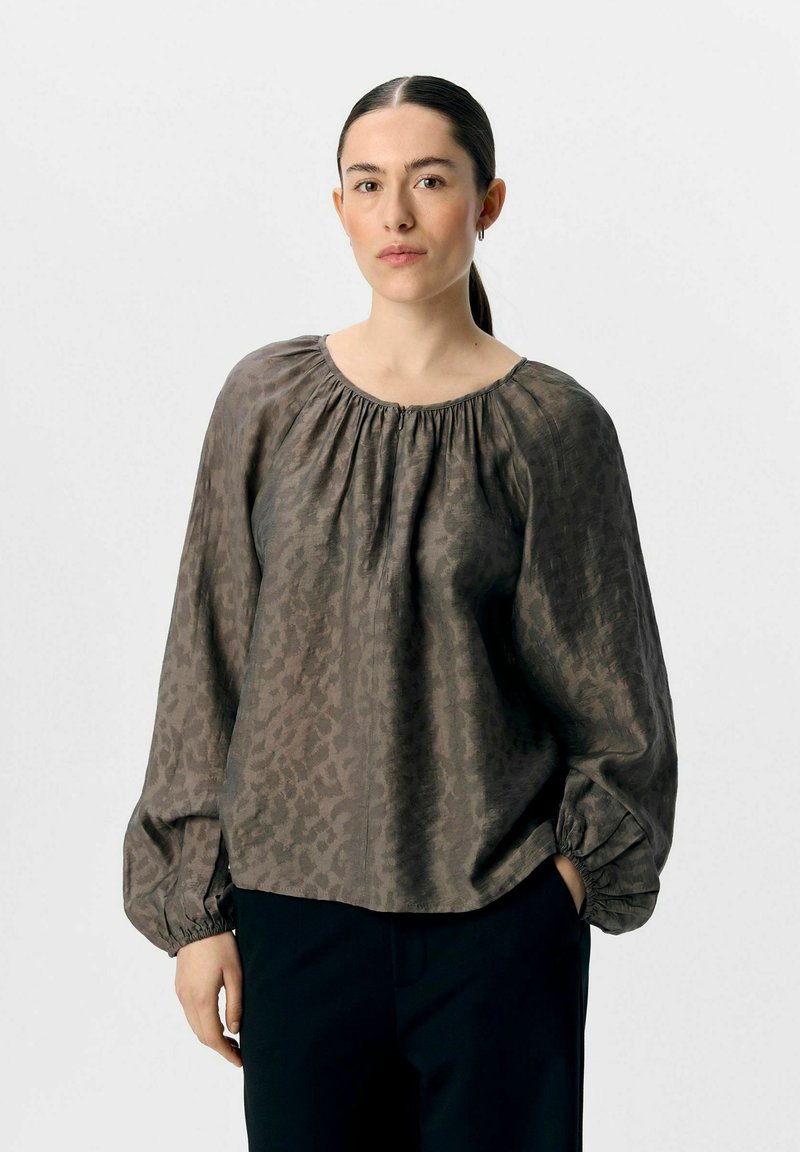 Blouse légère marron avec un imprimé léopard subtil, encolure froncée et manches ballon. Assortie à un pantalon sombre, texture lisse.
