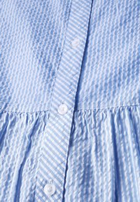 Camicia in cotone azzurro chiaro con righe verticali, dotata di un frontale con bottoni, texture arricciata all'orlo e bottoni bianchi.