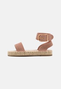 Sandalo in suede rosa con cinturini larghi e una fibbia alla caviglia. Presenta una suola in juta intrecciata e un fondo in gomma piatta.
