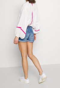Blusa blanca de manga abullonada con detalles en rosa, combinada con pantalones cortos de mezclilla. Los pantalones cortos están remangados y el conjunto se completa con zapatillas blancas.