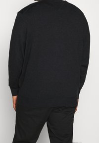 Pull en maille gris foncé à manches longues, poignets et ourlet côtelés, avec un col rond et une finition texturée subtile.