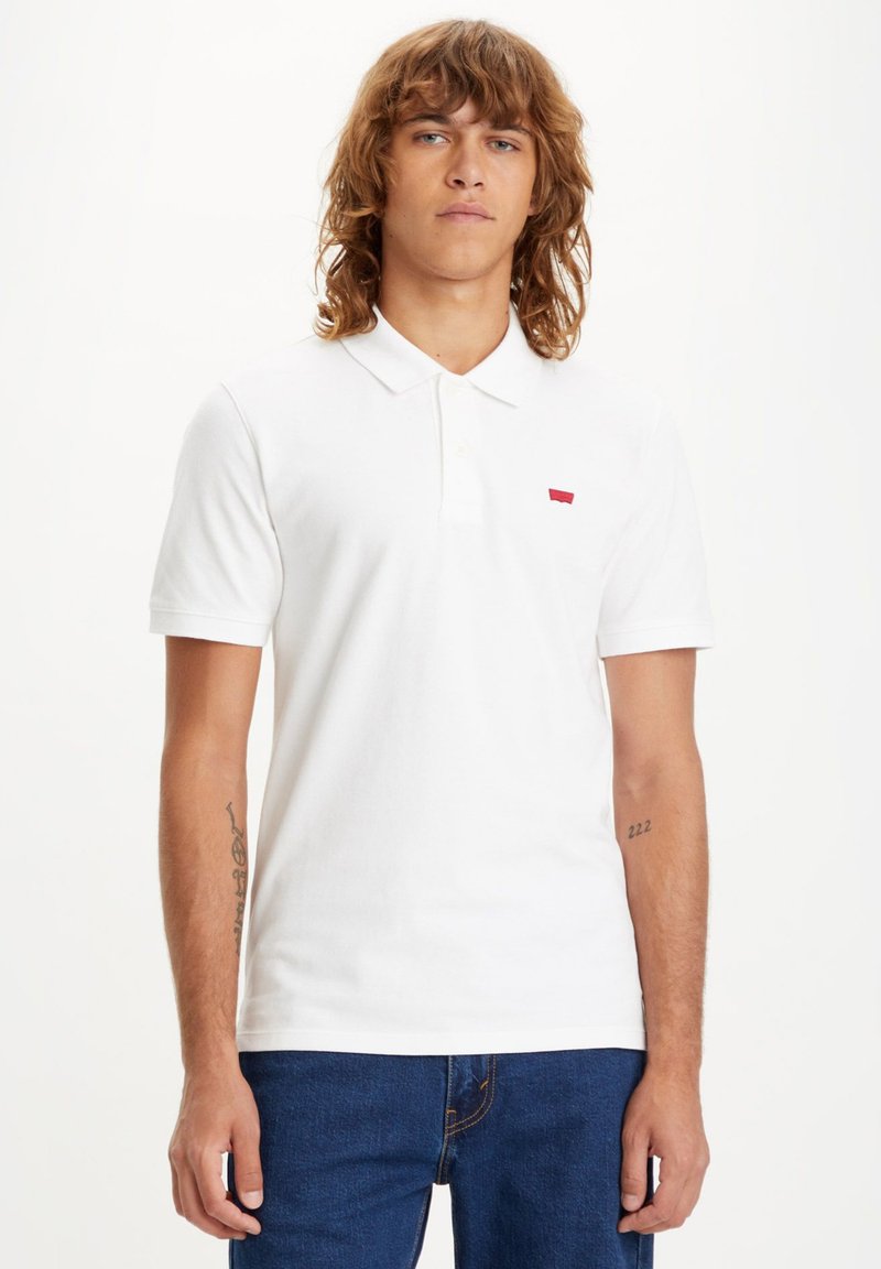 White polo shirt made of cotton, featuring a collar and short sleeves. Notable red logo on the left chest area. Classic fit design.