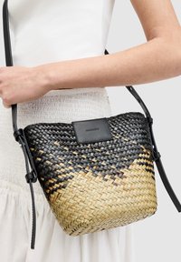 Woven handbag w kolorze gradientu od czerni do brązu, z gładką czarną skórzaną metką oraz regulowanym paskiem do wszechstronnego noszenia.