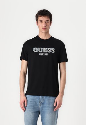 Black cotton t-shirt featuring the word "GUESS" in multicolored text and "EST. 1981" below. Short sleeves and crew neckline.