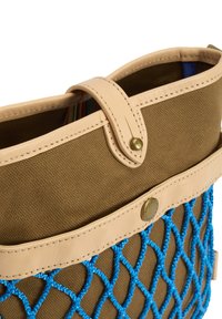 Καφέ υφασμάτινη τσάντα με μπεζ δερμάτινες λεπτομέρειες και λουρί, διακοσμημένη με μπλε δίχτυ και μεταλλικά καρφιά.