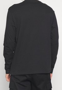 Schwarzes Langarmshirt mit Rundhalsausschnitt. Weicher, glatter Stoff. Gerade geschnitten mit einem Saum, der auf Hüfthöhe fällt. Einfaches Design, keine Grafik.