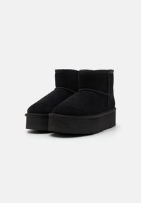 Botas de tobillo de ante negro con una suela de plataforma gruesa, punta redondeada y detalle de costura en la parte lateral. Textura suave y sin acentos de hardware visibles.