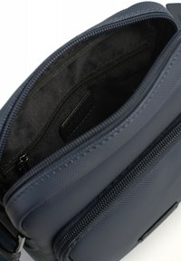Borsa a spalla blu navy con un esterno testurizzato, una tasca principale con zip e una tasca interna con chiusura a zip.