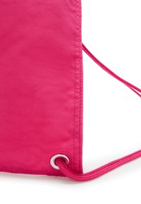 Angolo di un sacchetto con cordino, in tessuto rosa brillante, con un occhiello metallico che fissa un cordino rosa abbinato.