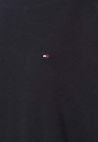 Sudadera de algodón negra de cuello redondo con un pequeño logo bordado en rojo, blanco y azul, cerca del área del pecho izquierdo.