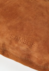 Borsa in suede marrone con bordi cuciti. Presenta il logo "SAMSOE" in rilievo. Texture liscia e finitura morbida, che mette in evidenza le variazioni naturali di colore.