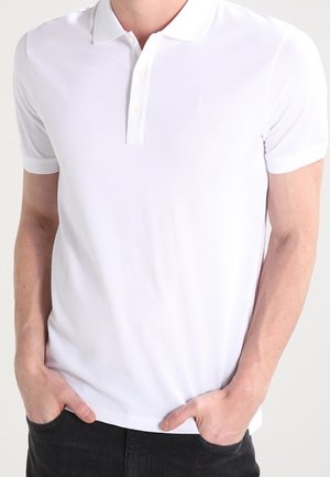 White polo shirt made of smooth fabric, featuring a classic collar, two-button placket, and short sleeves. Minimalist design with subtle branding.