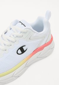 Scarpa sportiva bianca con tessuto testurizzato, caratterizzata da un logo nero, un design riflettente e una suola intermedia con gradiente rosa e giallo.
