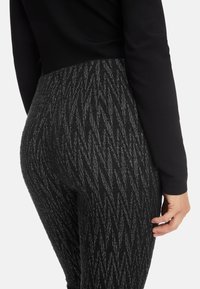Black textured leggings with a zigzag pattern and metallic accent threads; paired with a black fitted top. Shows side and rear view.