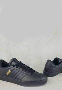 Czarne skórzane sneakersy z teksturowanym wykończeniem, sznurowanym przodem, trzema paseczkami oraz kontrastującym złotym logo. Niska sylwetka z zaokrąglonym czubkiem.