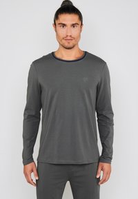 Grålangærmet skjorte med rund hals, med navyblåt kravebånd og et lille logo på brystet. Glat stoftekstur.