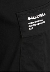 Svart tyg med en svart ficka som har vit text: "JACK & JONES URBAN ESSENTIALS hållbarhet och pålitlighet" samt koreanska tecken.