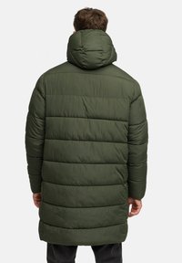 Groene gewatteerde jas met een hoge kraag en horizontale stikdetails. Kenmerkt zich door een gestructureerd oppervlak en een langere lengte.