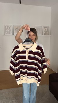 Camisola polo com riscas em castanho e creme, com colarinho e três botões. Ajuste solto, mangas curtas, e acentuada com riscas em azul claro.