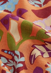 Tissu coloré avec un motif floral dans des tons orange, vert, violet et bleu ; aspect texturé, léger et tissé.