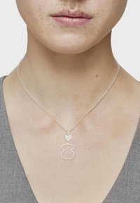 Collar de plata con un colgante en forma de corazón sobre un contorno en forma de oso. La cadena es delicada y está unida estrechamente.