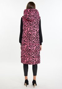 Lang puffer vest med et pink og sort zebra-print, der har en stor hætte, kviltet design og sorte leggings. Båret med sorte hæle.