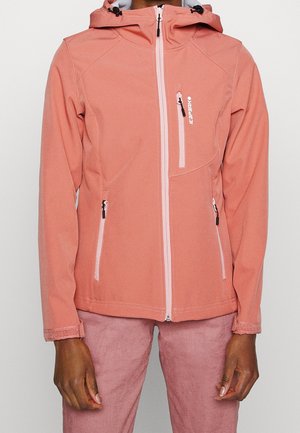 Persoon die een roze softshell jas met ritssluiting en capuchon draagt, en bijpassende roze broek, staand tegen een effen lichte achtergrond.