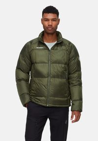 Dunkelgrüne Pufferjacke mit Reißverschluss vorne. Mit horizontalen Steppabschnitten, hohem Kragen und subtiler Logo auf der linken Seite.