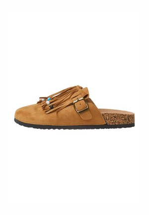 Chaussure en suède marron à enfiler avec franges et perles décoratives. Dispose d'une semelle en liège et d'une semelle en caoutchouc texturé pour une meilleure adhérence.