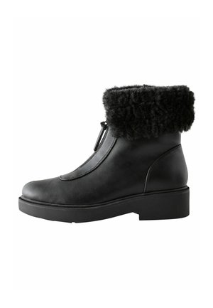 Bottine en cuir noir avec un col en fausse fourrure noire texturée, détail de fermeture éclair sur le côté et un petit talon bloc pour la stabilité.