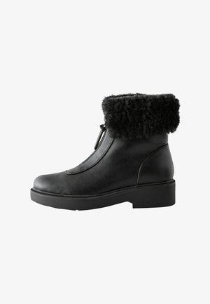 Black leather ankle boot with a textured black faux fur cuff, side zipper detail, and a low block heel for stability.