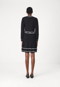 Robe noire côtelée avec un corsage ajusté et une jupe évasée, rehaussée de rayures blanches au bord et à la ceinture, ainsi que des manches longues.