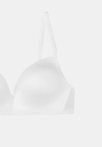Soutien-gorge blanc rembourré avec bretelles réglables, tissu lisse et conception sans couture. Présente un logo discret sur les bretelles pour le branding.