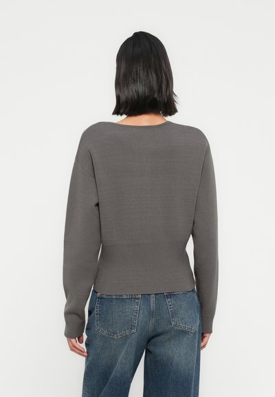 Pull gris tricoté avec ourlet et poignets côtelés, doté d'une coupe décontractée. Porté avec un jean en denim bleu taille haute.