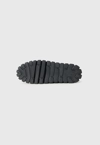 Suela de zapato de goma negra con una superficie texturizada, que presenta surcos profundos y ranuras con patrón para tracción y soporte.