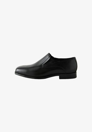 Zapato de vestir negro de cuero sin cordones con tacón bajo y costuras visibles, mostrado de lado sobre un fondo blanco.