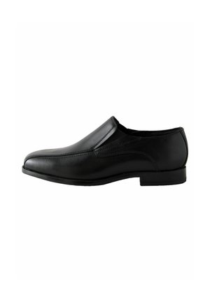 Chaussure noire en cuir à enfiler avec une texture lisse, un bout arrondi et des détails de couture minimaux. La semelle basse et plate accentue un design épuré.