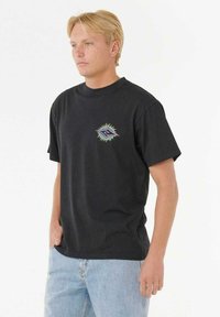 Sort bomulds t-shirt med korte ærmer, der har en farverig grafik på brystet, og en afslappet pasform, parret med lyseblå jeans.
